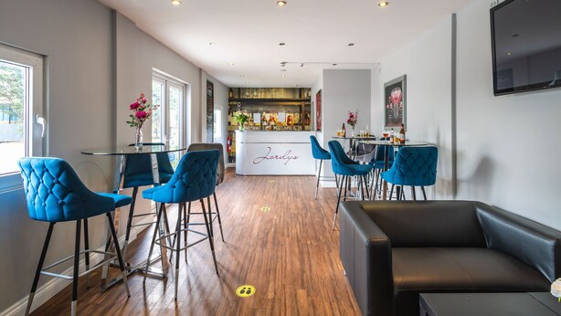 A modern bar area with blue bar stools, a black leather couch, and a bar counter with a sign reading "Lordys". - Peterborough by Verve (Peterborough)