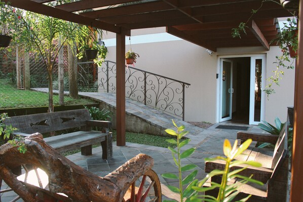 Un área de patio techada con un banco de madera, un banco de piedra y una barandilla metálica.