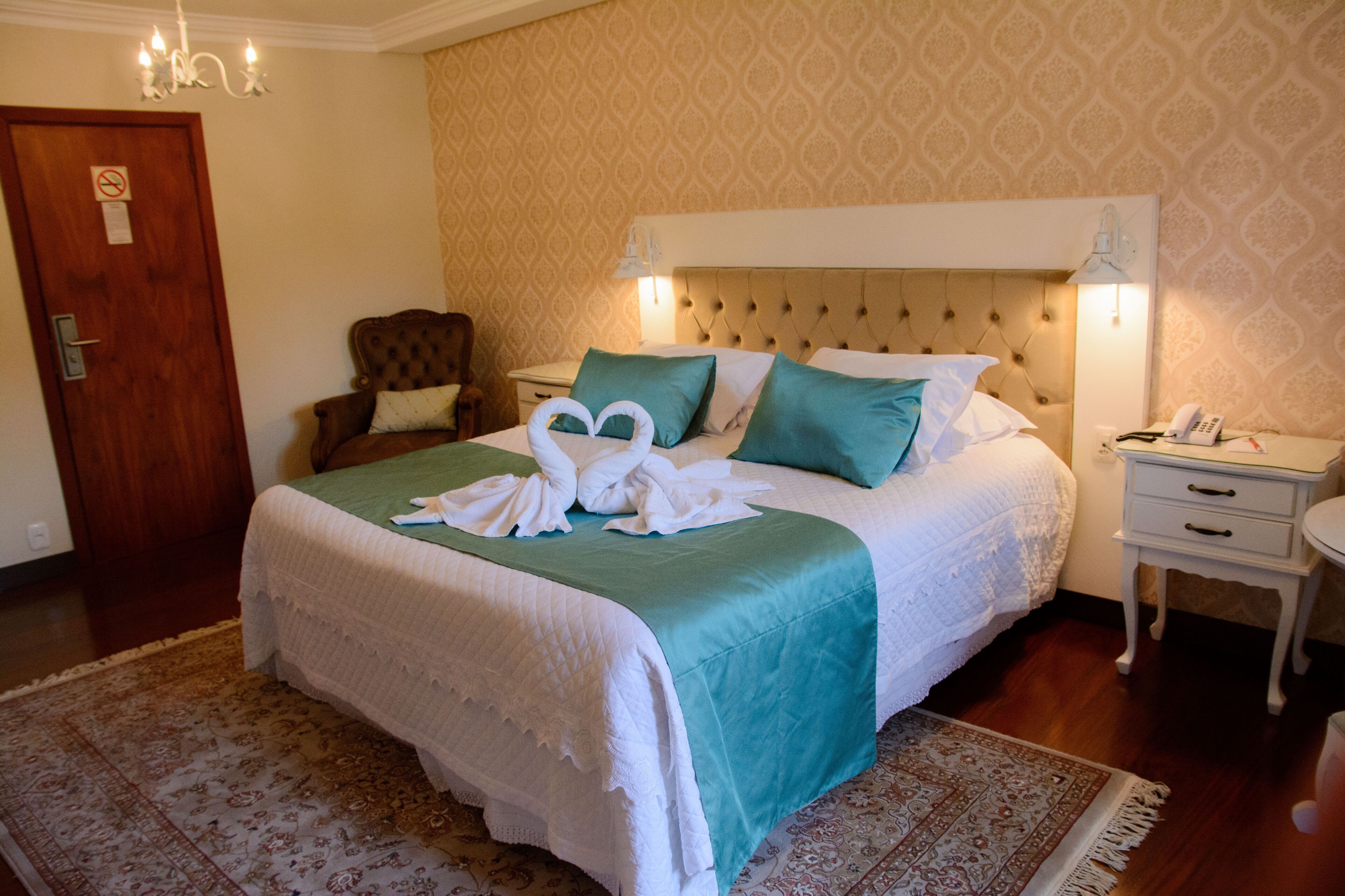 A neatly arranged hotel room with a large bed, a bedside table, a nightstand, and a door.