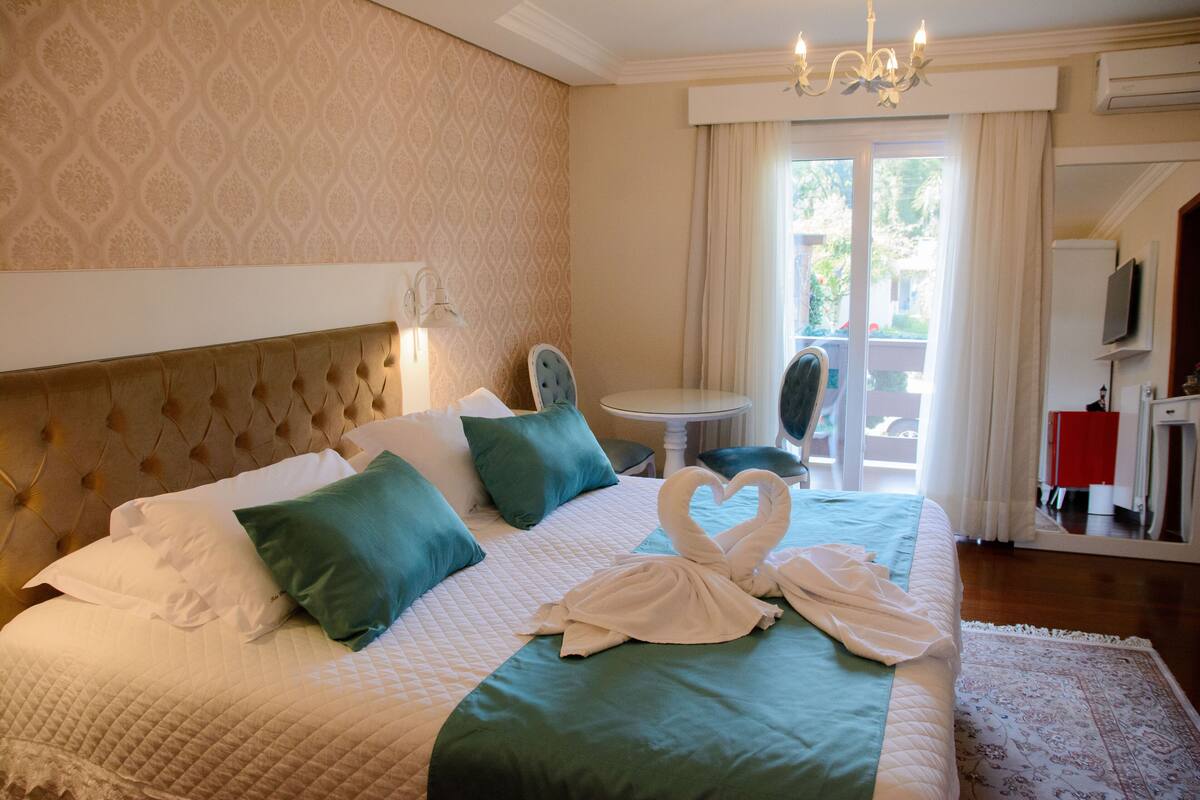 Ein Hotelzimmer mit einem großen Bett, einer Kandelaber, einem Esstisch und Blick ins Freie.