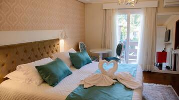 A hotel room with a large bed, a chandelier, a dining table, and a view of the outdoors.