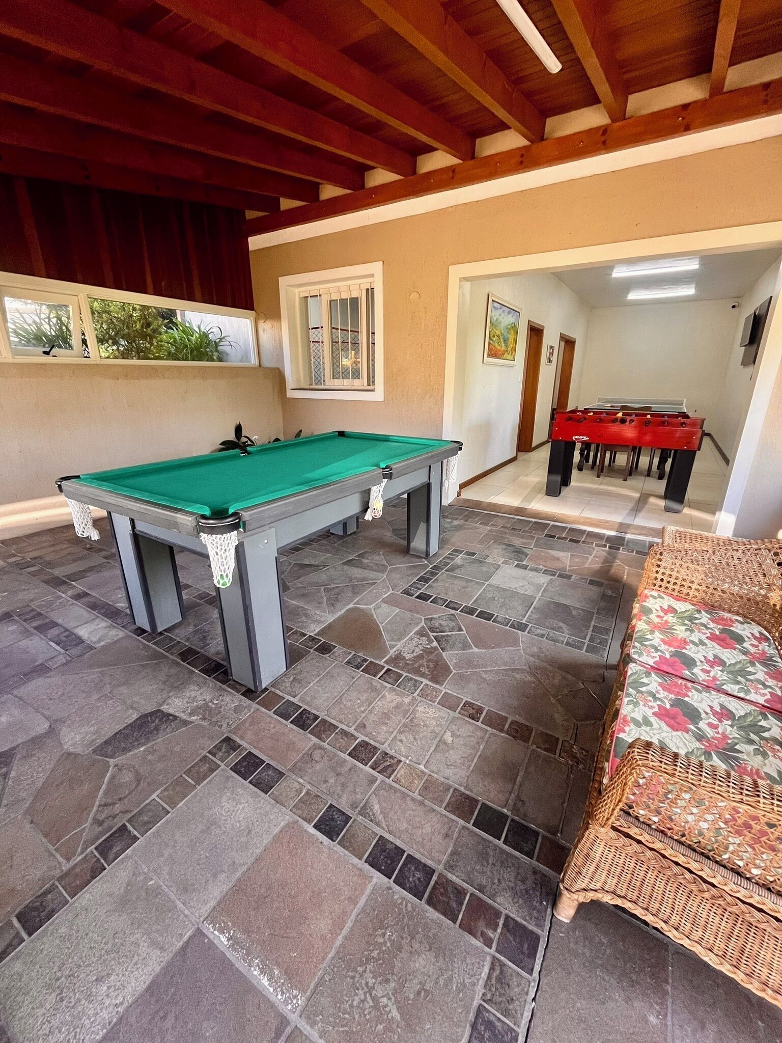 Una mesa de billar en una habitación con suelo de piedra y un sofá de mimbre.