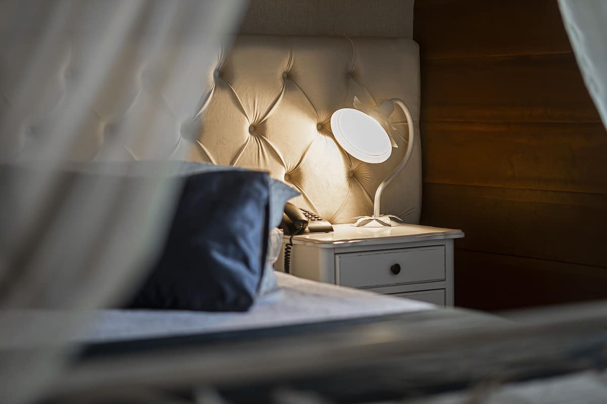 Ein Schlafzimmer mit Bett, Nachttisch, Lampe und Vorhängen.