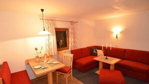 A cozy living room with a red sofa, a wooden dining table, and a small side table. - Haus Almfriede (Leutasch)