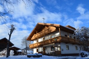 Un edificio de madera de dos pisos con balcones, un letrero que dice “Hotel Alpenhof” y nieve en el suelo.