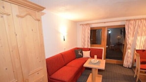 A cozy room with a red sofa, a small wooden table, and a wardrobe. - Haus Almfriede (Leutasch)