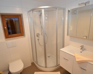 Un baño moderno con ducha envuelta en vidrio, inodoro, lavamanos con espejo y ventana de madera.