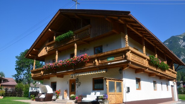 A traditional chalet with a balcony, a front porch, and a mountain backdrop. - Haus Almfriede (Leutasch)