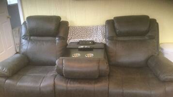 A brown leather sofa with a patterned throw pillow and a remote control on it.