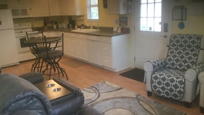 A compact living space with a kitchenette, a dining area with a table and chairs, a patterned armchair, and a sofa.
