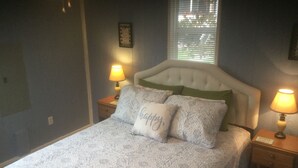 A bedroom with a bed, two bedside lamps, a window with blinds, and a wall clock.