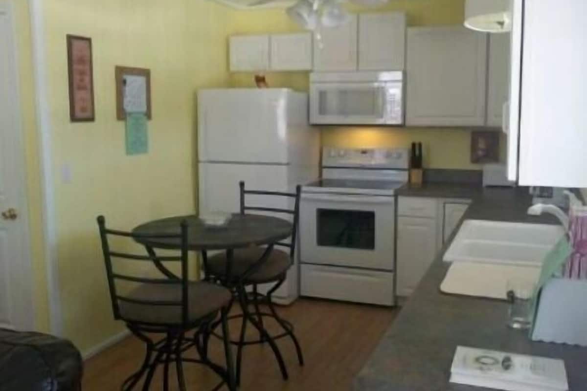 Cocina compacta con microondas, estufa y refrigerador. Hay una mesa de comedor con sillas y un ventilador de techo.