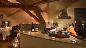 An interior with exposed wooden beams, a kitchen with a granite countertop, and a dining area with a table set for a meal. - Chez Maman (Geneva)