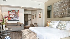 A modern hotel room with a large bed, a sofa, a small table, and a decorative painting. - Chez Maman (Geneva)