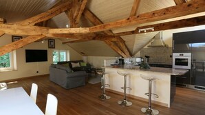 A spacious loft-style living area with a kitchen and dining space, featuring exposed wooden beams and a large window. - Chez Maman (Geneva)