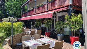 An outdoor dining area with tables and chairs, surrounded by greenery and a red awning. - Chez Maman (Geneva)