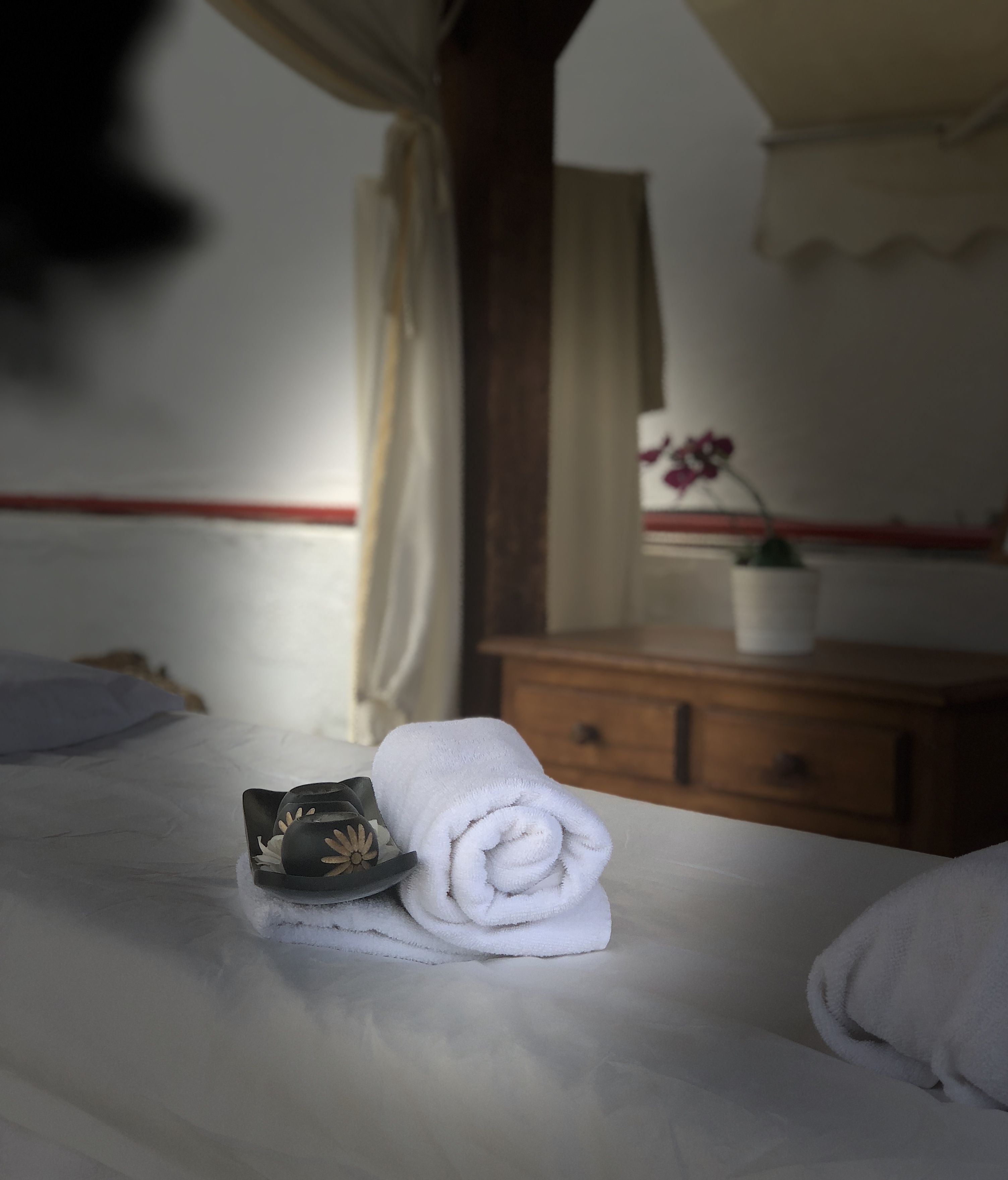 A neatly made bed with a rolled white towel and a decorative item on it.