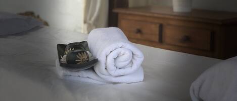 A neatly made bed with a rolled white towel and a decorative item on it.