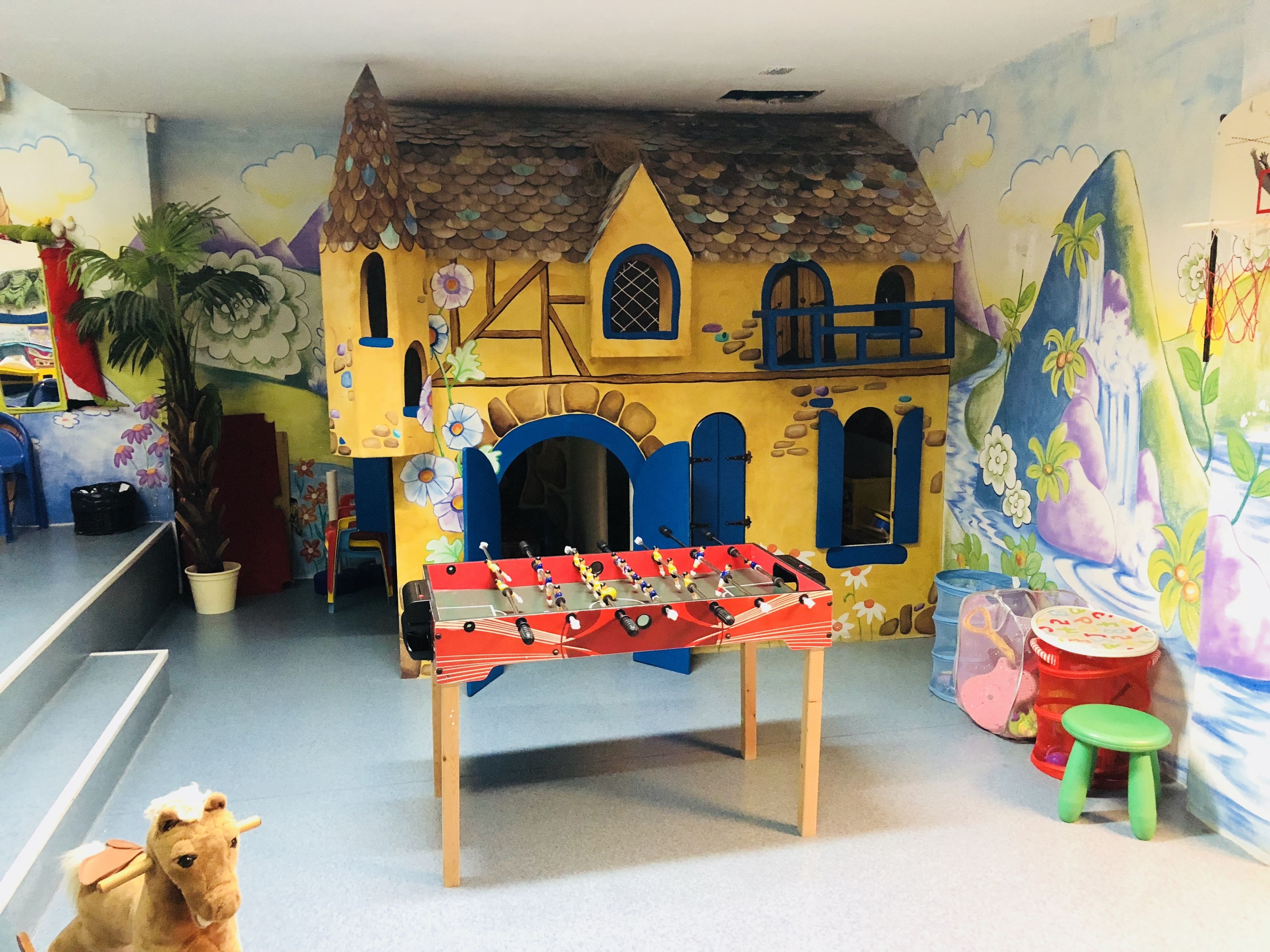 Une pièce avec une table de baby-foot, une petite figurine de cheval et une fresque représentant une maison aux couleurs vives.