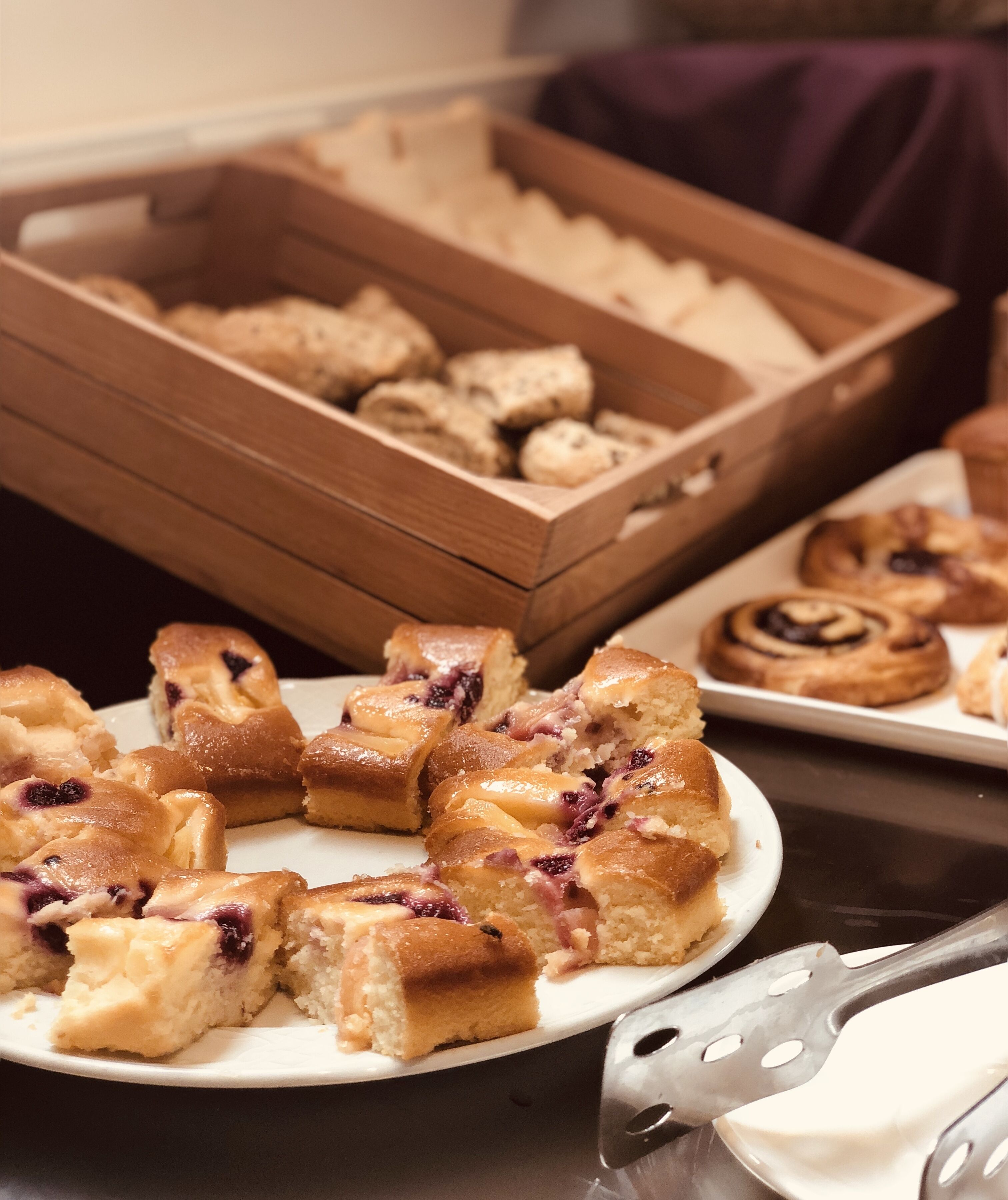 Een tafel met diverse gebakken producten, waaronder gebak en brood, gepresenteerd op borden en in een houten doos.