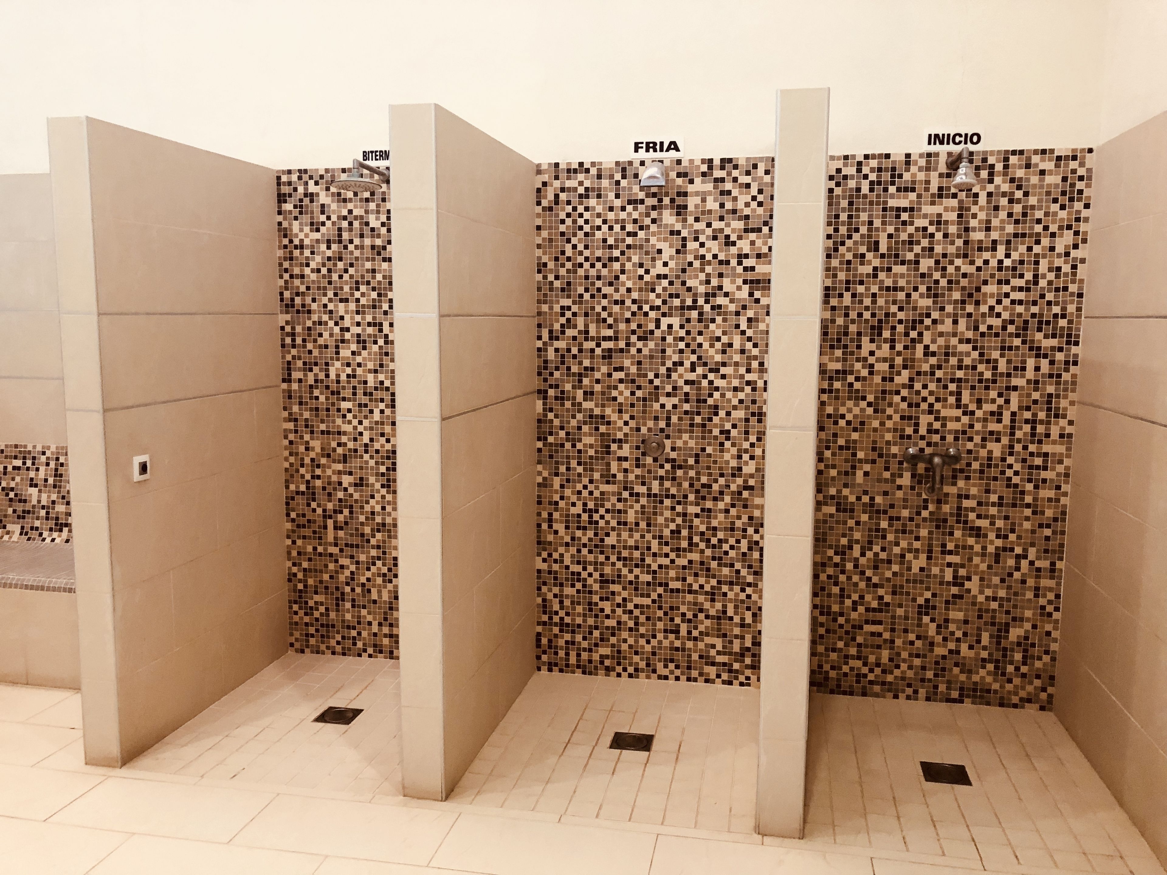 A row of three shower stalls with mosaic tile walls and a tiled floor.