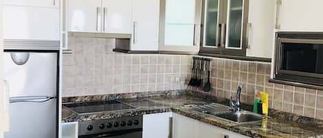 Una cocina moderna con armarios blancos, encimera de granito, electrodomésticos de acero inoxidable y horno empotrado.