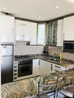 Μια σύγχρονη κουζίνα με λευκά ντουλάπια, πάγκο από γρανίτη, συσκευές από ανοξείδωτο ατσάλι και εντοιχισμένο φούρνο.
