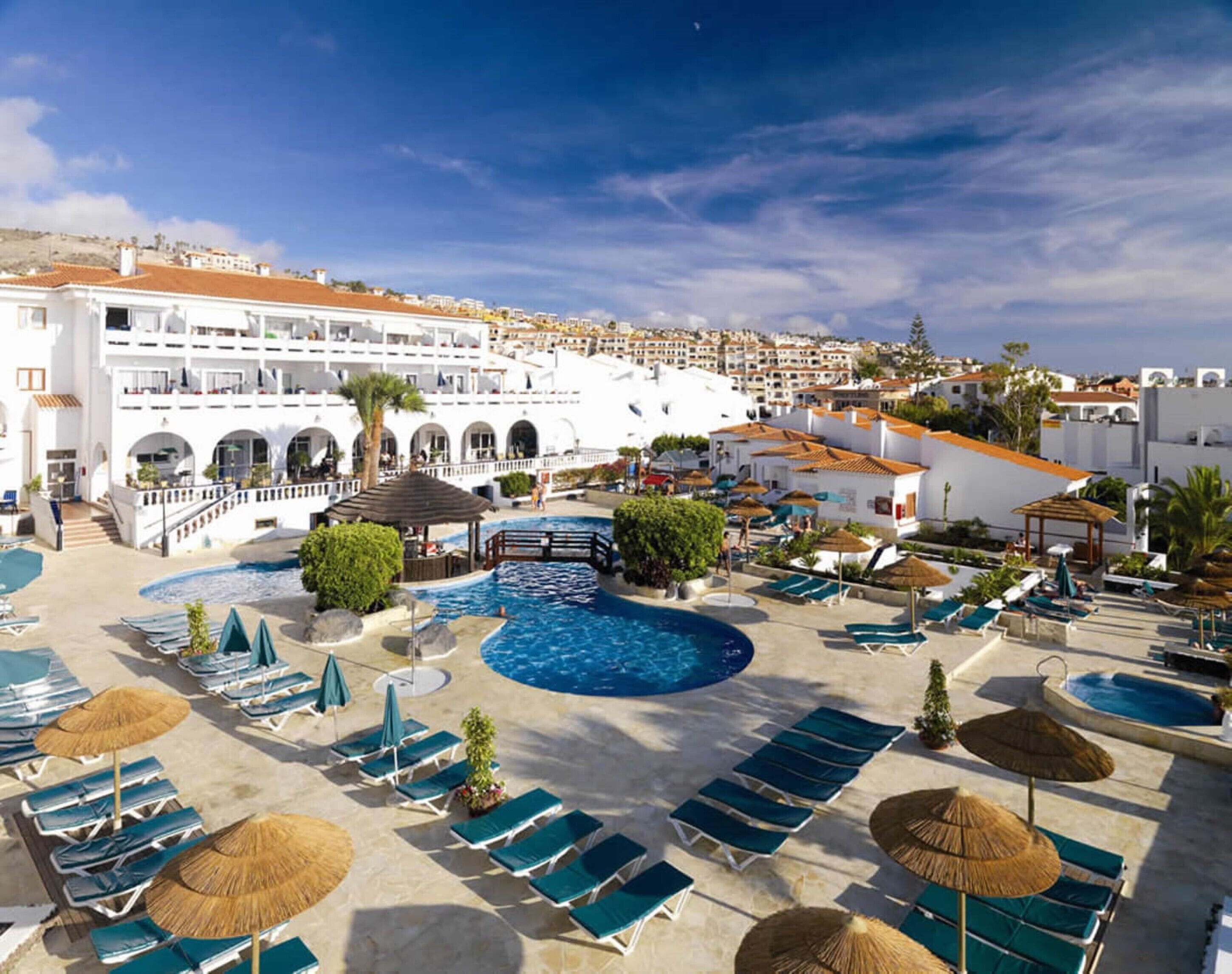 A resort with multiple swimming pools, sun loungers, and a large building with balconies.