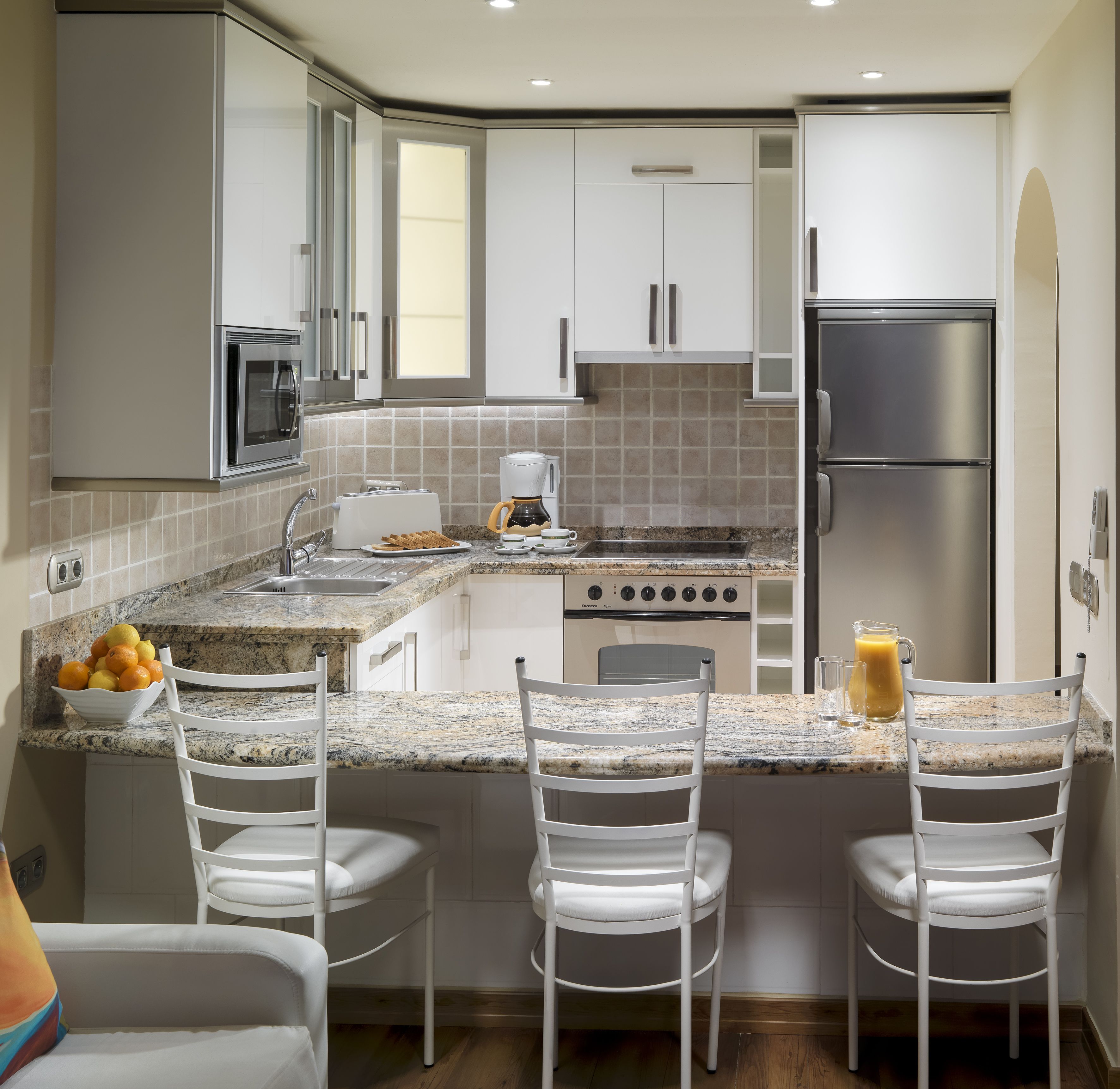 A modern kitchen with white cabinetry, a built-in oven, a coffee maker, and a fruit bowl on the counter.