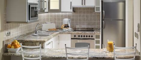 A modern kitchen with white cabinetry, a built-in oven, a coffee maker, and a fruit bowl on the counter.