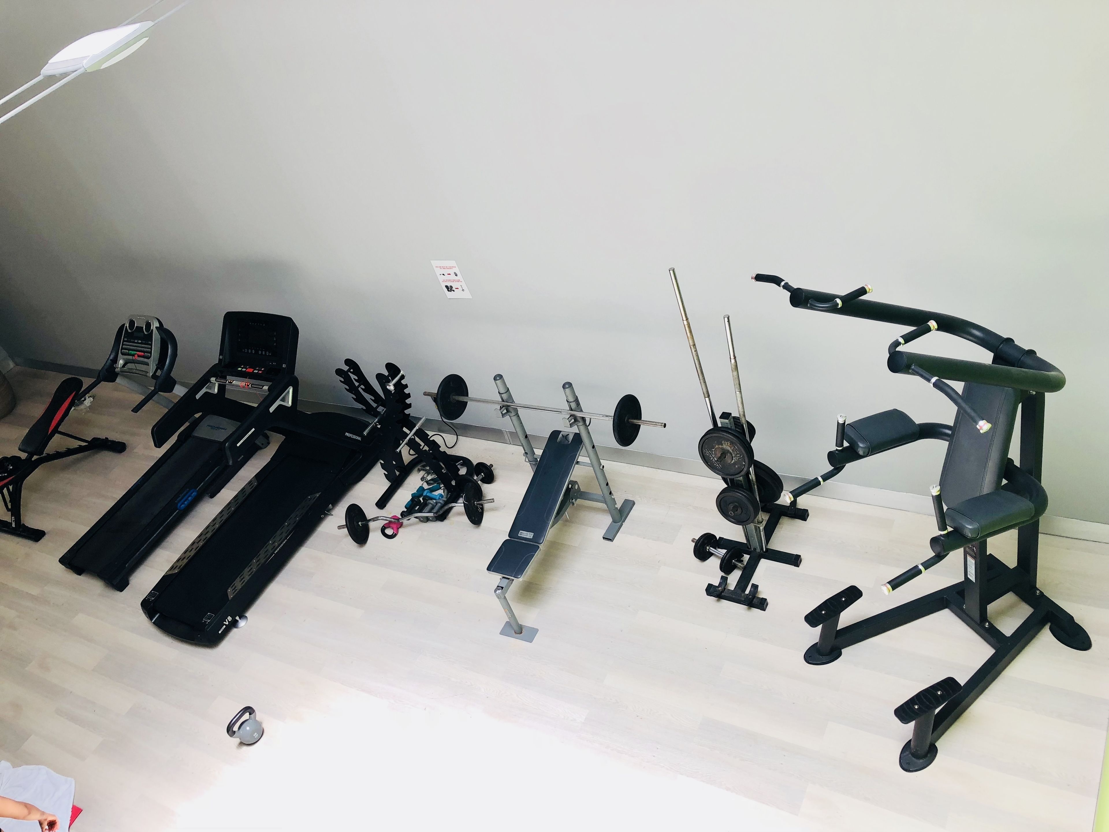 Een huisgym met een loopband, een bankdrukapparaat, gewichten en een hometrainer.