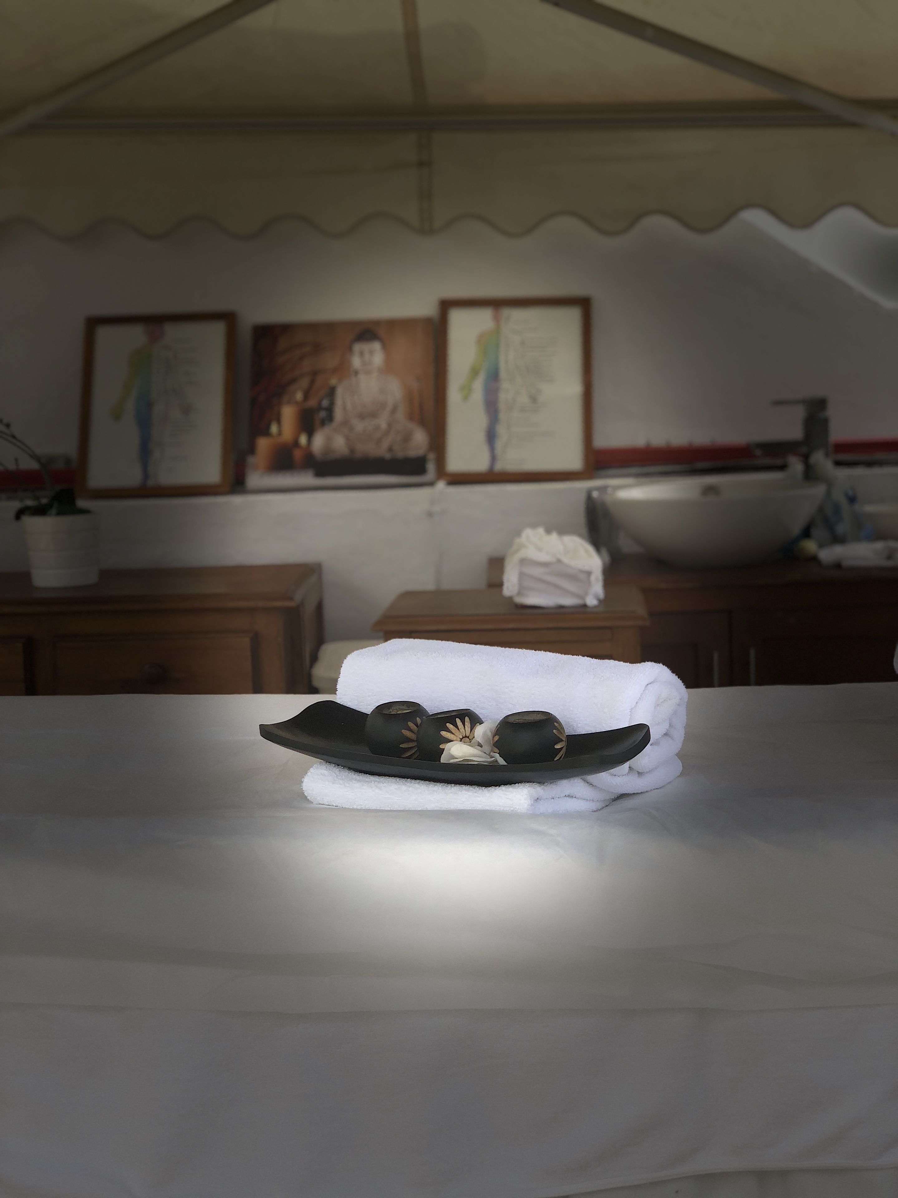 A neatly made bed with a towel and a black tray with three bowls, a white sink, and two framed pictures on the wall.