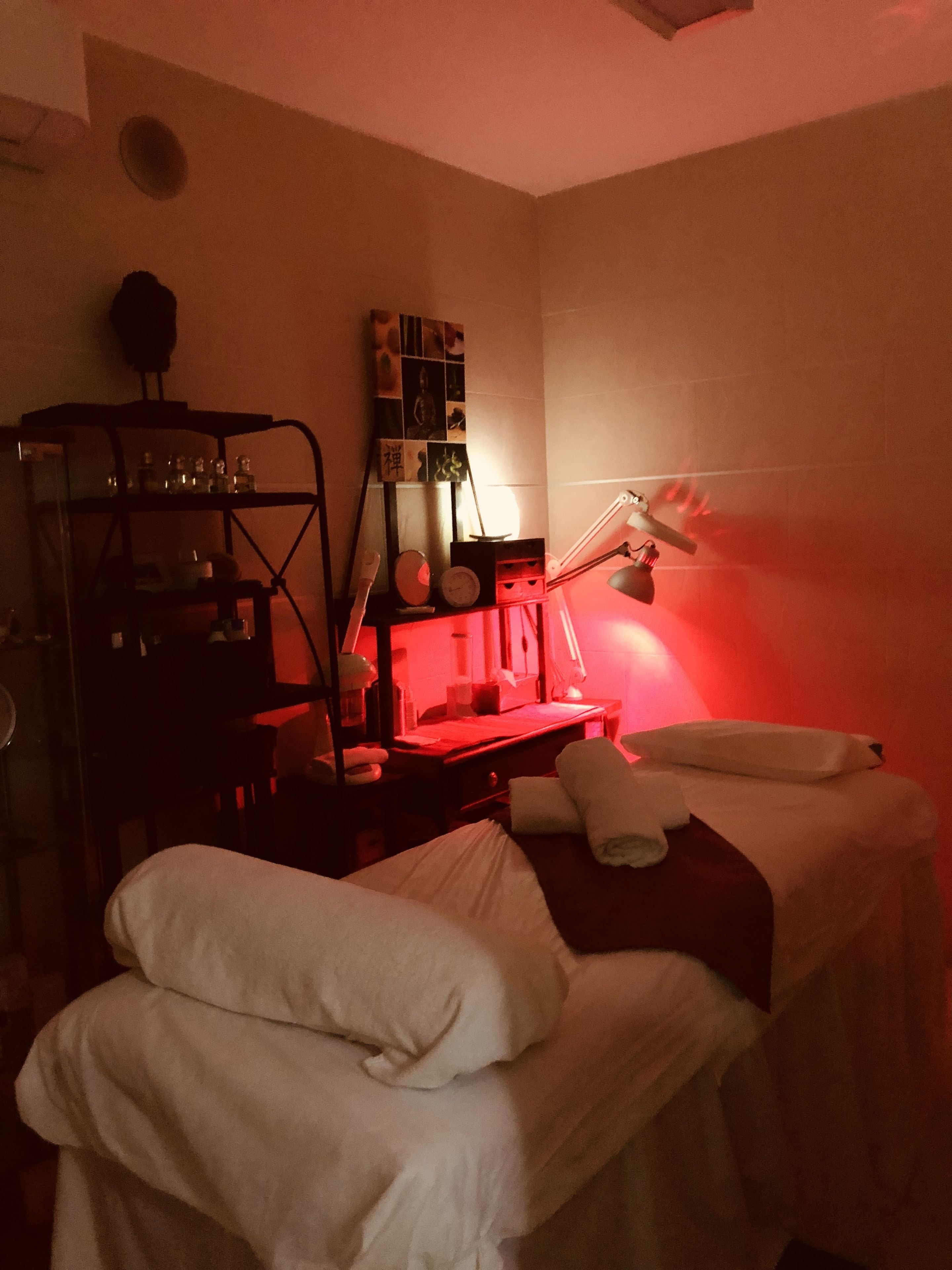 Una habitació poc il·luminada amb dos llits, un escriptori amb una làmpada i una estant amb diversos objectes.