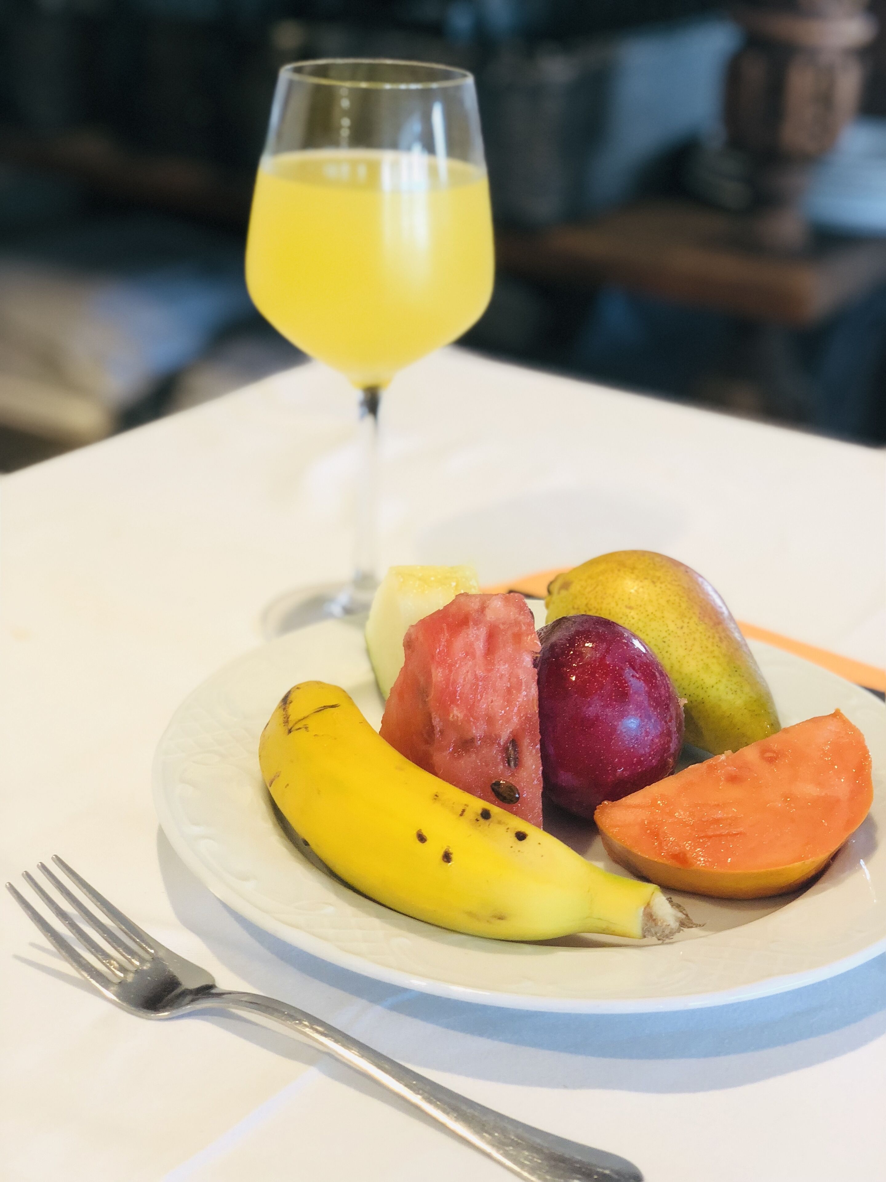 A plate of fruit and a glass of orange juice on a white table.