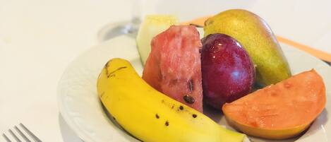 A plate of fruit and a glass of orange juice on a white table.