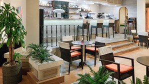 Een moderne barruimte met rieten stoelen en tafels, een toonbank met verschillende flessen en een grote potplant.
