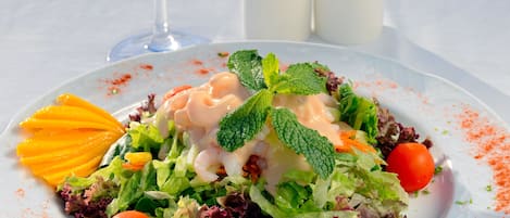 Une assiette blanche contenant une salade, un verre de vin blanc, ainsi que des salières et des poivrières posés sur une table.