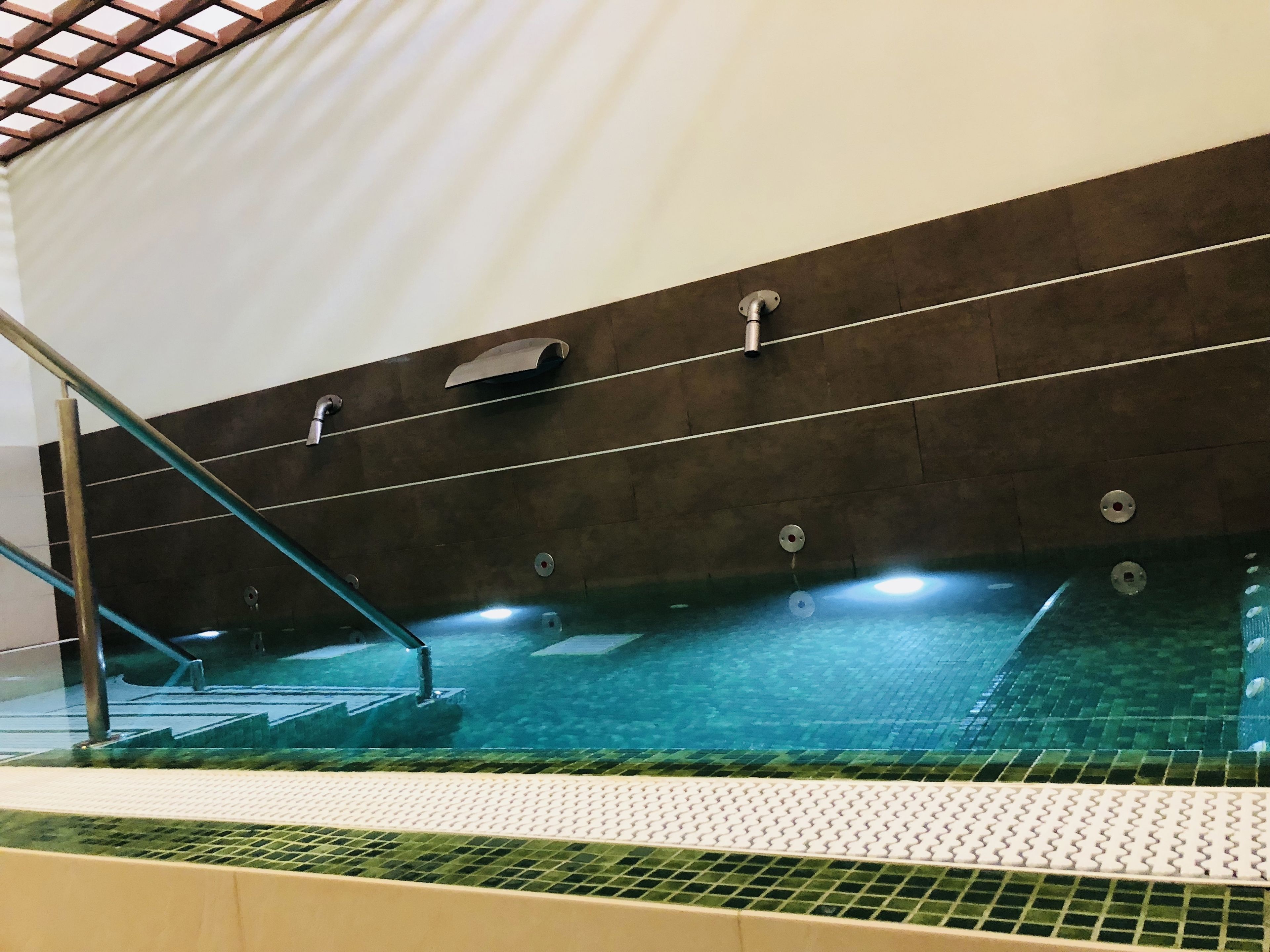 Una piscina interior con agua cristalina, suelo de baldosas y barandilla de metal.