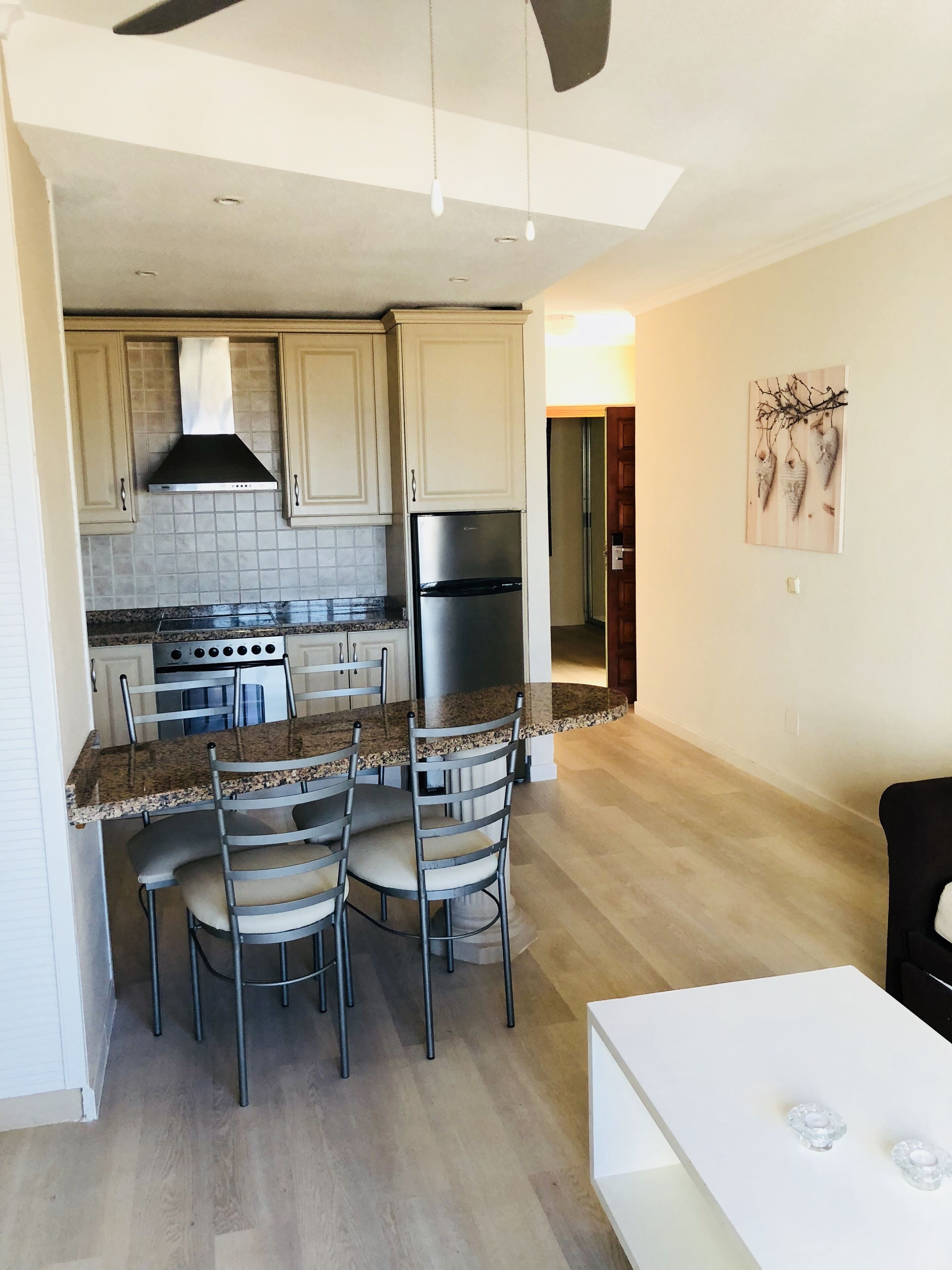 Een moderne keuken met granieten aanrecht, roestvrijstalen apparatuur en een eethoek met een witte tafel en metalen stoelen.