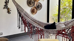 A hammock in a room with a large window, a wall-mounted hat rack, and a patterned rug.