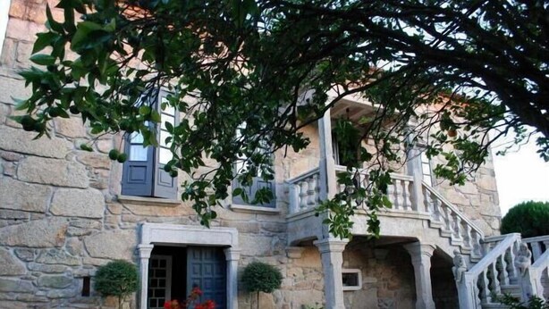 A stone building with a blue door, potted plants, and a staircase. - Pazo Carrasqueira (Ribadumia)