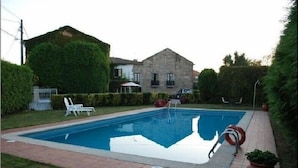 A rectangular swimming pool with a clear blue water surface, surrounded by a brick pathway. There are white lounge chairs and a red lifebuoy near the pool. - Pazo Carrasqueira (Ribadumia)