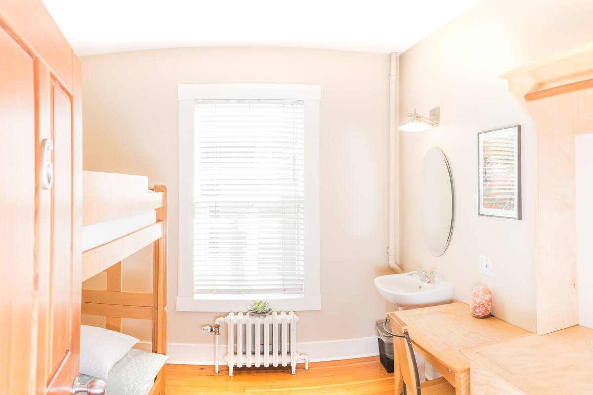 A bedroom with a bunk bed, a radiator, a window with blinds, a sink, and a mirror.