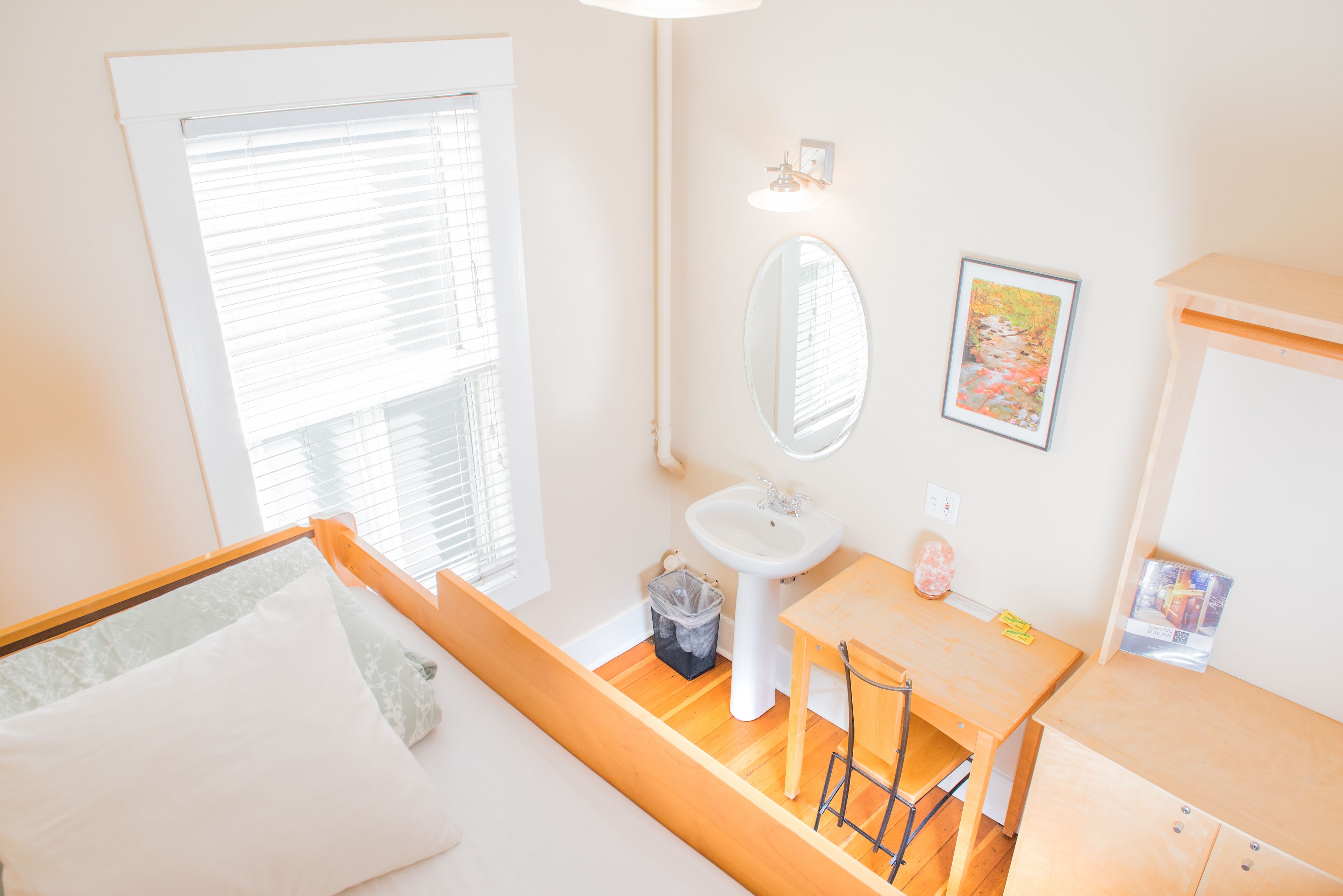 Habitación de hotel con una cama, un escritorio de madera, un lavamanos y una ventana con persianas.