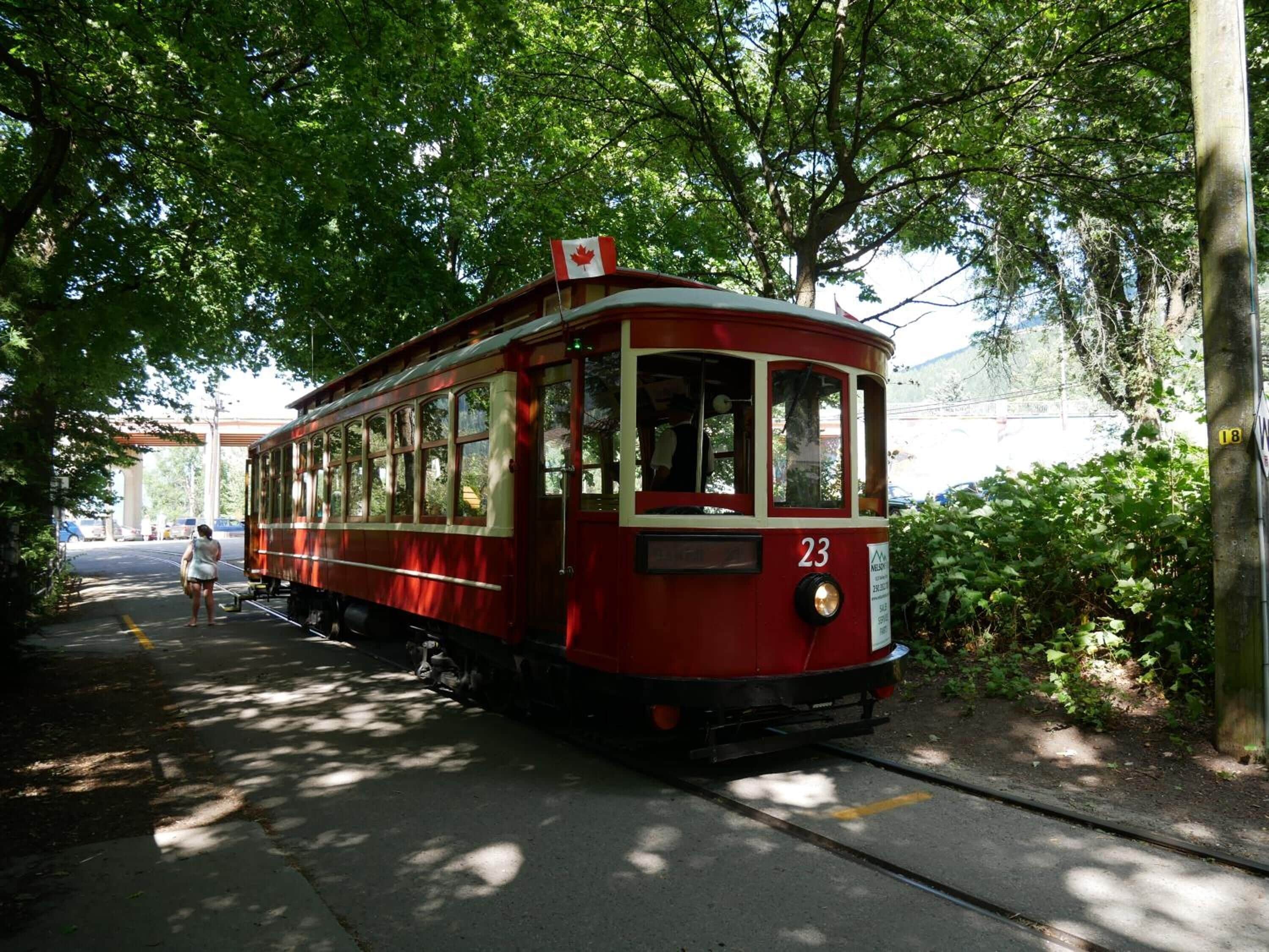 Un tranvía rojo con el número 23, estacionado sobre rieles, rodeado de árboles y follaje.