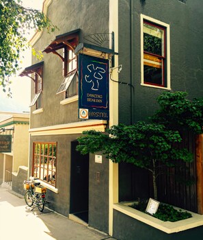 A building with a sign for Dancing Bear Inn Hostel, a bicycle parked outside, and a small garden area. - Dancing Bear Inn Hostel (Nelson)