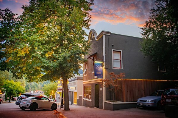 A building with a sign for a restaurant, a tree in front, and parked cars. - Dancing Bear Inn Hostel (Nelson)