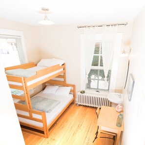 A bunk bed room with a radiator, a window with curtains, and a small table with a bottle. - Dancing Bear Inn Hostel (Nelson)