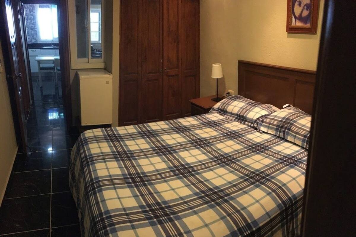 Quarto com cama, mesa de cabeceira, abajur e armário de madeira.