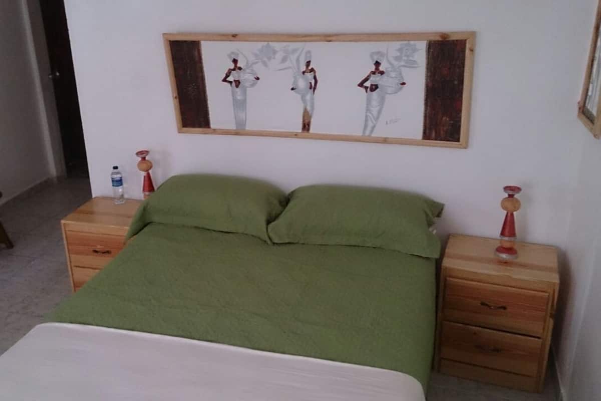 Quarto com cama, duas mesas de cabeceira, uma cadeira e um quadro na parede.